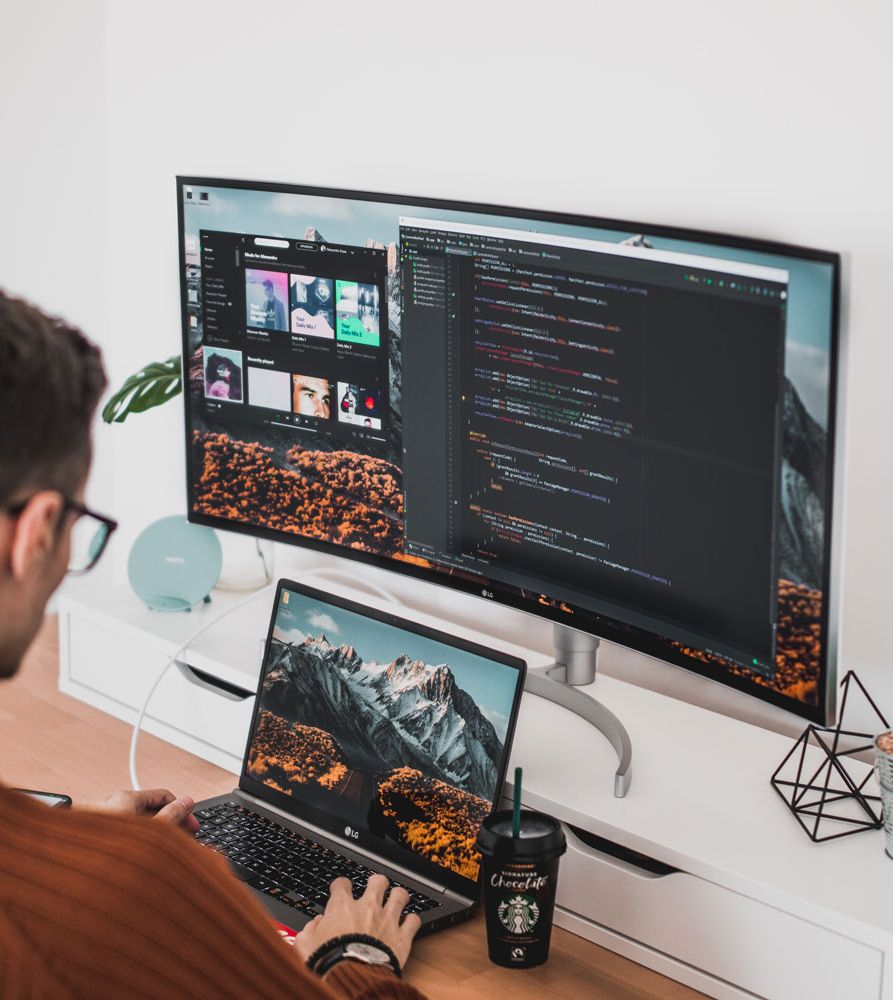 A developer working across a laptop and large monitor